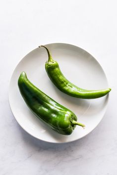 two green peppers sitting on top of a white plate