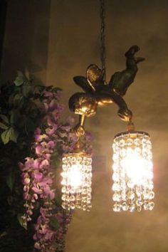 a chandelier with three lights hanging from it's sides and purple flowers in the background