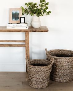 two wicker baskets sitting on top of a wooden table next to a white vase