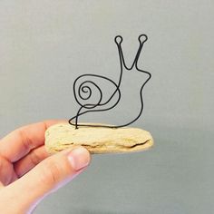 a hand holding a piece of wood with a wire snail on it's back