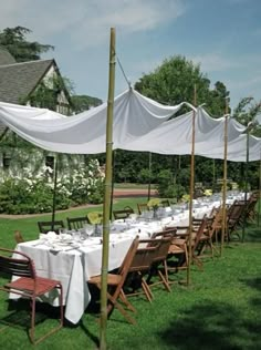 an outdoor dining area with tables and chairs covered in white cloths, surrounded by lush green grass