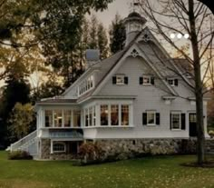 a large white house sitting on top of a lush green field next to a forest