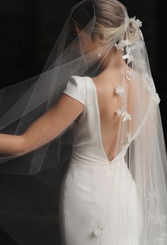 the back of a bride's wedding dress with a veil over her shoulder and flowers on it