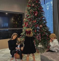 two women and a child sitting in front of a christmas tree