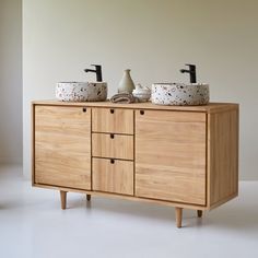 two bowls are sitting on top of a wooden cabinet that has drawers and handles, along with soap dispensers