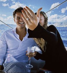 a man and woman sitting on a boat with their hands in the air while holding wine glasses