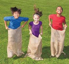 three children are standing in the grass with their hands on their hipss and one is holding a sack