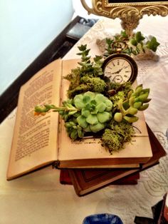 an open book sitting on top of a table next to a clock and planter