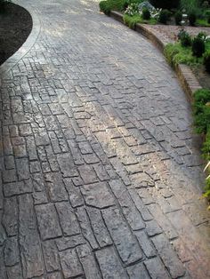 an empty brick road with trees and bushes in the background