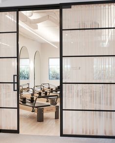 an open glass door leading to a salon with mirrors on the wall and benches in front of it