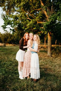 three young women standing next to each other in the grass