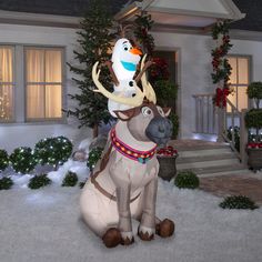 a large inflatable reindeer sitting on top of a snow covered ground next to a house