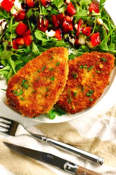 two pieces of fried fish on a plate with a salad and fork next to it