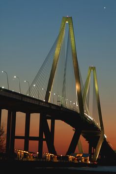 the bridge is lit up at night with lights shining on it's sides and in the foreground