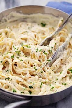 a close up of a pan of food with noodles and parsley on the side