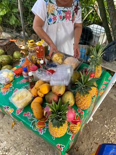 a woman cutting up fruit on top of a green picnic table covered in pineapples