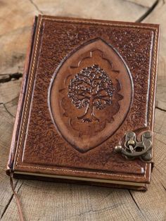 a leather book with a tree on it sitting on top of a piece of wood