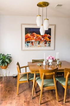 a dining room table with green chairs and a painting on the wall above it,