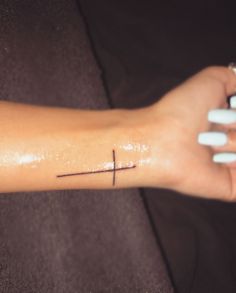 a woman's arm with a small cross tattoo on the left side of her arm