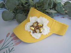 ALL ORDERS TOTALING OVER $35 SHIP FREE I designed this adorable unique yellow sun visor making an ivory flower and added a beaded shell flower accent to the center. Very Unique and cute. Perfect for the beach. Visor has velcro back. \See more hats and visor here: https://www.etsy.com/shop/theraggedyrose?ref=seller-platform-mcnav&section_id=10557807 Custom orders alway welcome. Thanks for visiting my shop. Adjustable Gold Mini Hats For Spring, Adjustable Gold Visor Hat, Gold Brimmed Mini Hats For Spring, Spring Gold Brimmed Mini Hats, Brimmed Sun Hat For Spring, Adjustable Yellow Mini Hats For Kentucky Derby, Adjustable Sun Hat For Spring Gift, Gold Baseball Cap For Summer, Handmade Yellow Sun Hat For Spring