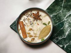 a bowl filled with food and spices on top of a green table cloth next to an orange slice