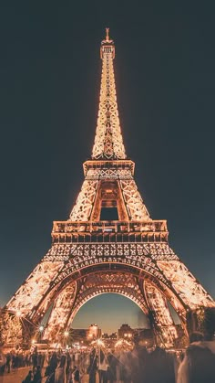 the eiffel tower lit up at night with people standing around in front of it