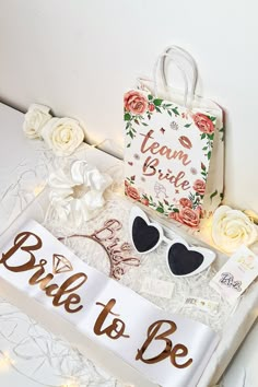 the bride to be sign is next to her sunglasses and wedding gift bag, along with some flowers