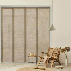 a living room with a chair, rug and window coverings in shades of beige