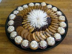 a platter filled with cupcakes and cookies on top of a wooden table