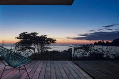 a chair sitting on top of a wooden deck next to a tree covered hillside at sunset