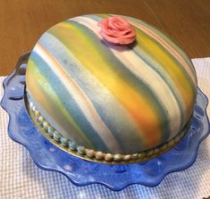 a multicolored cake with a rose on top sitting on a blue platter