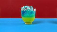 two glasses filled with liquid and ice on top of a blue table next to each other