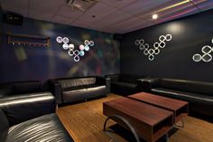 a room with black leather couches and wooden tables in front of the wall has circles painted on it