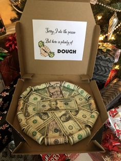 a pizza in a box with money on the inside and some christmas presents around it