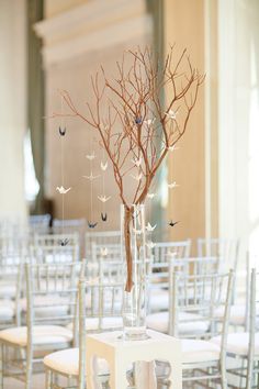 a vase with branches and birds hanging from it is sitting on a table in front of rows of chairs