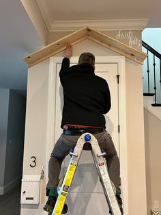 a man standing on top of a ladder next to a white door in a room