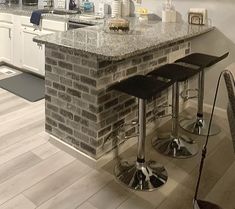 two stools sit in front of a brick bar with marble counter tops and white cabinets