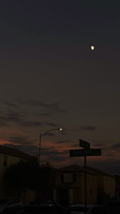 the moon is setting over some houses and street signs