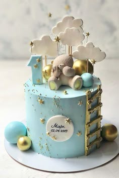 a blue and gold baby's first birthday cake with a teddy bear on top