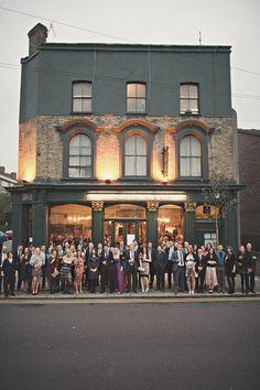 a large group of people standing in front of a building on the side of the road