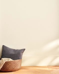 a pillow on the floor in front of a white wall with a basket underneath it