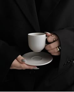 a woman holding a white cup and saucer in her right hand with gold nails