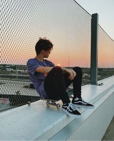 a young man sitting on the edge of a building with his skateboard in hand