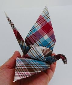 a hand holding an origami bird in plaid fabric