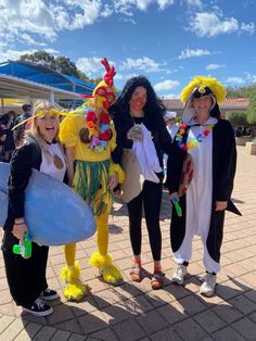 three women dressed in costumes standing next to each other on a brick walkway with blue sky and clouds behind them