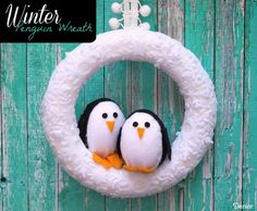 two penguins sitting in a wreath hanging on a wooden wall