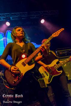 two women playing guitars on stage at a music festival, one woman is holding an electric guitar