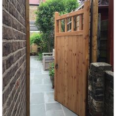 an open wooden door on a brick wall in front of a stone walkway and shrubbery