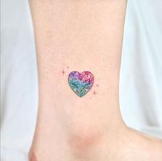 a heart shaped tattoo on the ankle with stars and watercolor paint splatters