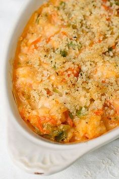 a casserole dish with cheese and vegetables in it sitting on a white cloth